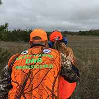 DNR Safety Training Classes Two people wearing orange practice firearm safety in a woodland prairie.