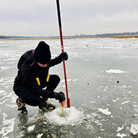 A person measuring the thickness of ice on a frozen lake