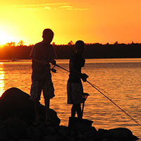 Regional fishing outlooks The sun creates a silhouette of two people fishing in a boat on a lake.