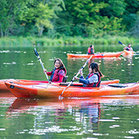 I Can! - outdoor skills programs for beginners A group of people enjoy paddling in orange kayaks on a lake.