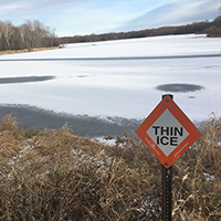 Ice and snowmobile safety. A sign next to a frozen lake warns visitors about thin ice.