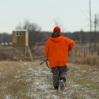 A youth, wearing orange, hunting in a field.